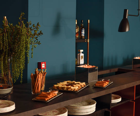  Elegant Mezzanine bar at The Excelsior Hotel set for cocktails and tea, featuring a spread of savory snacks, breadsticks, dipping sauces, floral decor, ambient candles, and a sophisticated drinks selection against a deep blue backdrop