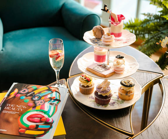 Afternoon tea at Excelsior Hotel with fashion-inspired pastries, champagne, and Dior art book on stylish table setting