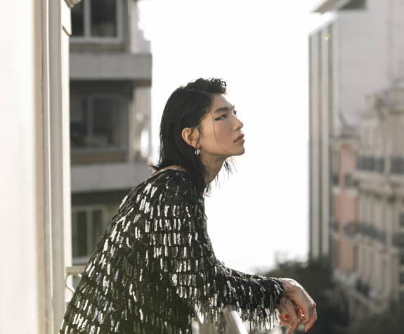 Fashionable guest in sparkling black dress enjoying the view from Excelsior Hotel balcony overlooking city buildings
