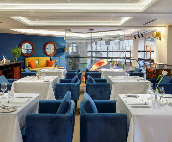 Sophisticated Mezzanine setup at The Excelsior Hotel for meetings or business lunches, featuring blue velvet chairs, white tablecloths, minimalist table settings, and a stylish, well-lit ambiance