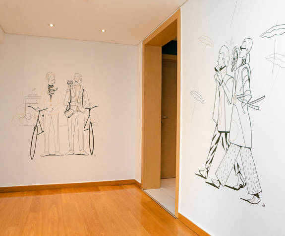 Contemporary line art murals in Excelsior Hotel corridor: one features fashionable couple walking with umbrellas, the other two men with bicycles and a puppy